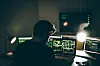 One man, sitting indoors surounded by computers, hacking crime is in motion, rear view.