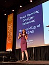 Kvinne holder foredrag på en scene foran en skjerm med teksten «Threat Modeling Developer Behaviour».