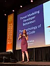 Kvinne holder foredrag på en scene foran en skjerm med teksten «Threat Modeling Developer Behaviour».